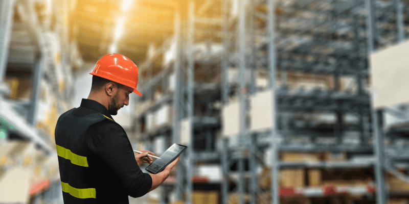 Supply chain manager standing in a warehouse checking inventory on a tablet