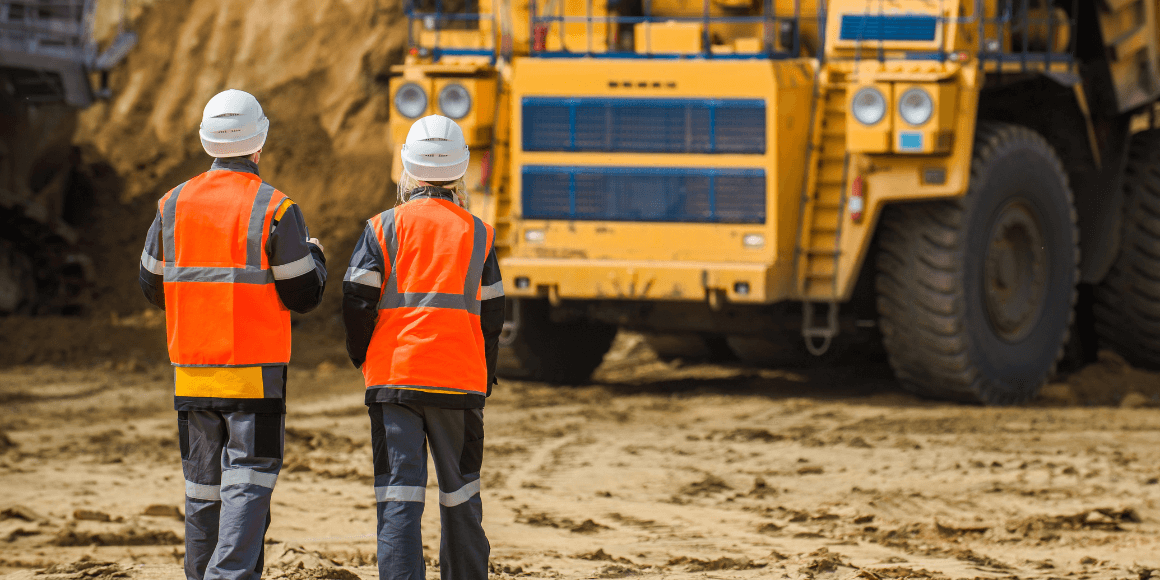 Two workers standing in an open pit in front of a mine truck